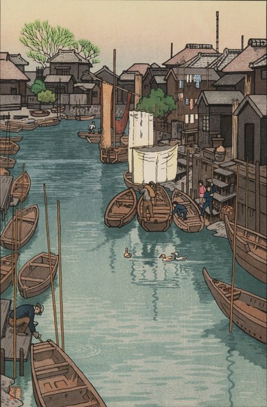 A scene looking along a narrow canal on an overcast summer's day in Urayasu, Chiba. Small 'bekabune' style wooden boats are moored on either side of the canal, while houses crowd in close to the water's edge. On our left, a male figure is tying up a boat; up ahead, another male figure and three kids clamber into their own boat. A trio of ducks swims along the middle of the canal. Overhead, the sky is dingy and overcast.