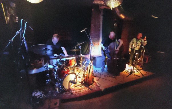 Arashi: 
from left to right: Paal Nilssen-Love playing drums, Johan Berthling playing double bass, Akira Sakata talking, pointing his finger in the air