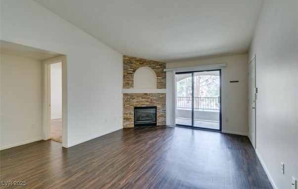From a home listing in Henderson Nevada, a ln empty living room with a gas hearth in the corner next to a sliding glass door to a small patio balcony.