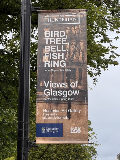 Banner hanging from a lamppost with trees and sky behind. Text reads:

The Huntarian
BIRD,
TREE,
BELL,
FISH, 
RING

June-September 2025
Views of Glasgow
Winter 2025-Spring 2026
Hunterian Art Gallery
Free entry
gla.ac.uk/hunterian
University of Glasgow
