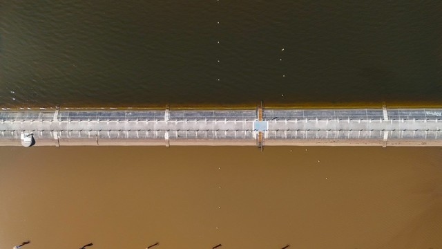 Parrearra Weir from directly above.  One one side of the weir, the water is a light, bright muddy brown, and on the other side it is a deep dark blackish colour. The weir divides the two colours sharply, creating an unusual and unexpected contrast of water colour