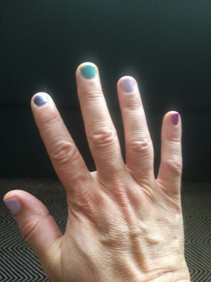 Right hand with different nail colors: light purple, dark blue with glitter, turquoise, another light purple, and pinkish purple.