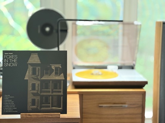 Jason Isbell - Foxes in the Snow LP cover.

An empty, old house on a black background. Artist and title upper left in white. Songs below in white.

The gold LP plays on a vintage, restored Bang & Olufsen Beogram 4000 linear-tracking turntable to the right.