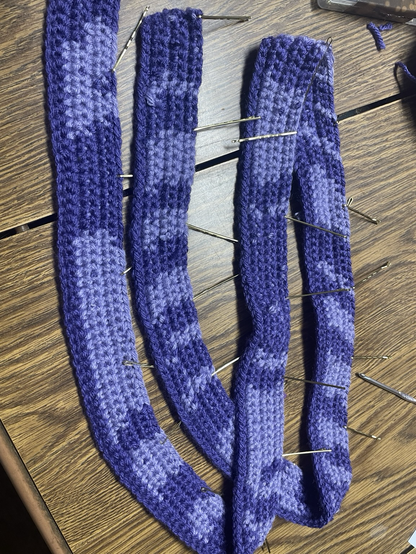 A long strand of crochet in two tones of purple, the pattern is striped of various lengths and widths.