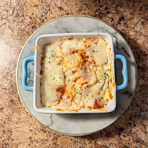 Image shows a blue baking pan on a gray marble plate filled with ravioli bake.