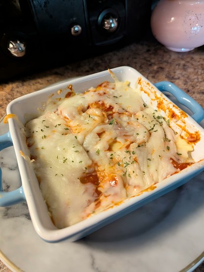 Image shows a close up of a blue baking pan on a gray marble plate filled with ravioli bake.