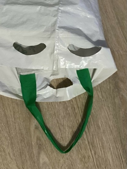 A plastic bag on the floor vaguely flattened, various holes near the top make it look like it has a dejected look on its face.