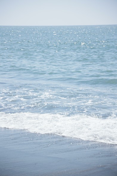A calm sea sparkling under sunlight, with gentle waves lapping against the shore, creating a serene coastal scene.