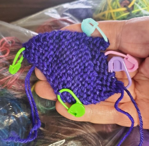 One half of a chickie wing in purple, with colorful stitch markers attached