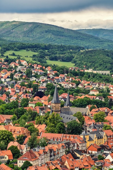 Blick von dem schloß Vorplatz auf die Stadt Wernigerode. Stadtdächer und dahinter die Berge und den Wolkenhimmel. In der Mitte der Szene ragt ein Kirchenturm hervor.