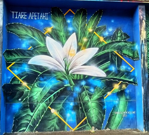 photo d'une peinture murale représentant une tiare apetahi, blanche, et des feuilles vertes sur un fond bleu.