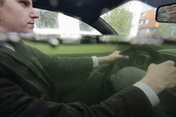 A picture of a young man in suit, steering a car while the water is reaching up to his chin. He is looking rather unimpressed with the situation.
