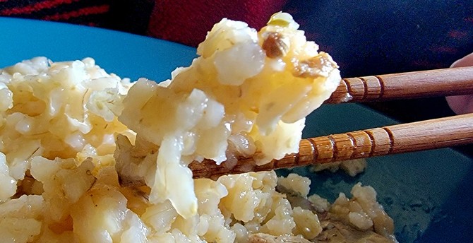 Clump of brown rice held in chopsticks, could be seen as a frog, or bear cub, or puppy