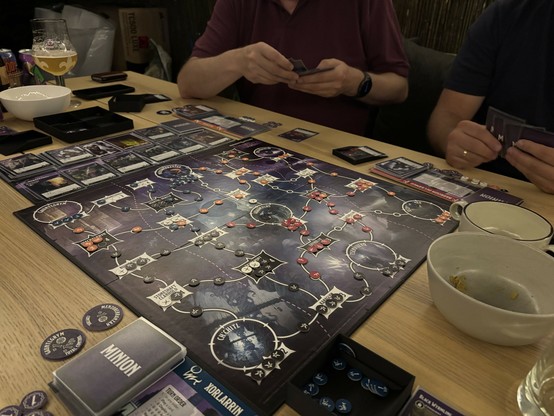 Tyrants of the Underdark, the boardgame in full effect. 2 players are sitting at the opposite side of the table and looking at their cards & options.