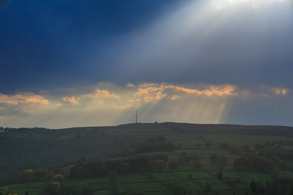 A green ridge line on which sits a large steel radio transmitter - shafts of sunlight shine down from grey clouds