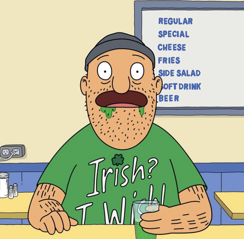 Teddy from Bob’s Burgers sits at the counter, eating his lunch in a green shirt with the green foam coming out of his mouth - the shirt reads Irish, I wish