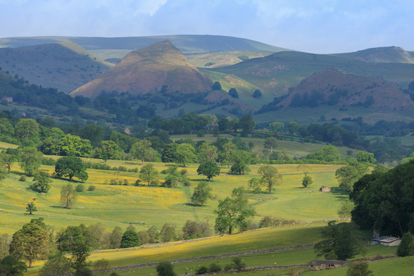 A view up a green valley mottled with yellow flowers and deciduous trees. 'Deciduous' .. there's a word that shows someones being a bit pompous isn't it. 'Leafy green' would be a far better word here wouln't it ?.. no hold on thats two words. Anyway, at the head of the valley are a set of pointy hills that if you really squint your eyes, take some mind altering drugs and also have a wildly weird imagination, just might resembled a sleeping dragon.  Maybe.