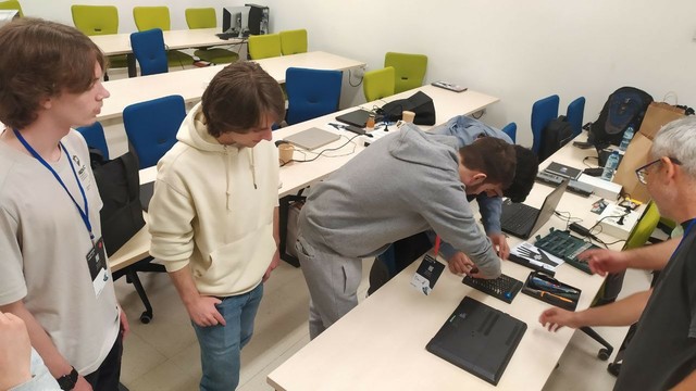 4 persoas novas cacharreando con ordenadores nun aula