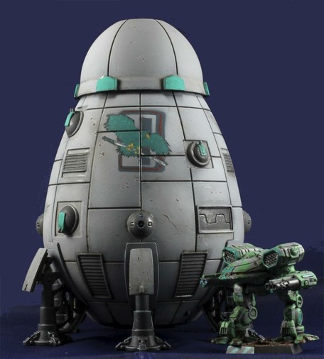 A grey Overlord-C standing behind a green-grey Turkina, against a dark blue background. Clan Jade Falcon insignia is prominently displayed on the upper hull. The miniature is seen from a low angle.