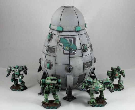 A grey Overlord-C standing behind a quartet of green-grey OmniMechs against a grey-white background. There's a Turkina, a Warhawk, an Ebon Jaguar and a Nova Cat. The Clan Jade Falcon insignia is prominently displayed on the upper hull. The miniature is seen from a slightly elevated angle.