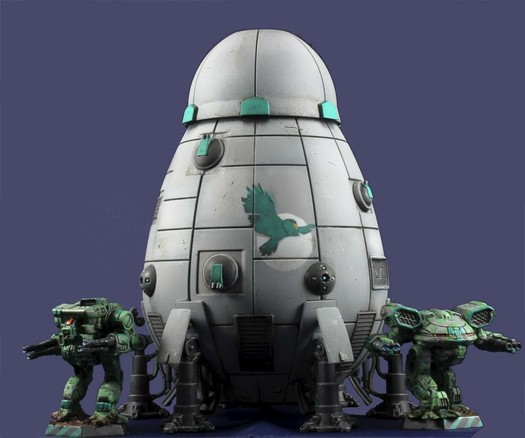 A grey Overlord-C standing flanked by a green-grey Turkina and a Warhawk, against a dark blue background. Clan Jade Falcon's Gamma Galaxy insignia is prominently displayed on the upper hull. The miniature is seen from a low angle.