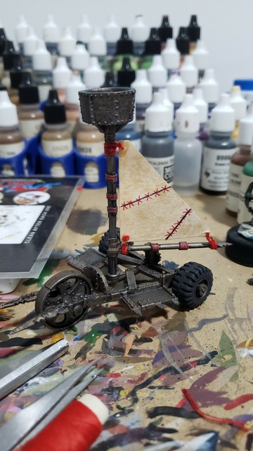 Ramshackle tri-wheeled scrap metal vehicle with a central mast and a triangle sail.