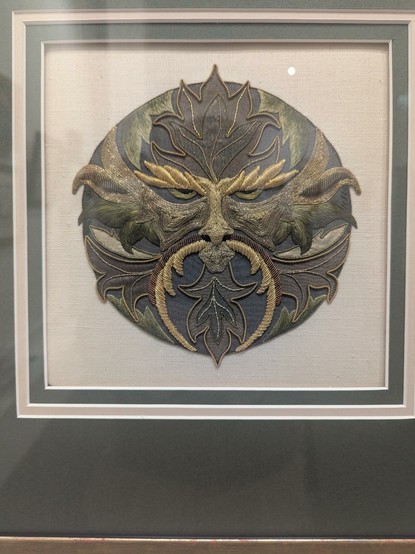 Needlework of a "greenman".  Made with delicate threads in green, bron and gold.