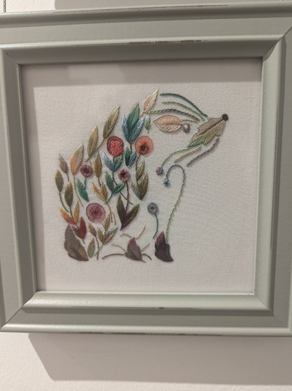 Photo of needle artwork showing a hedgehog compisee of separate smaller shapes of leaves and flowers.