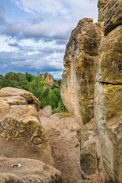 Blick durch die Sandstein Formationen. Am Horizont Wolkenhimmel und der Wald und weitere Felsen.