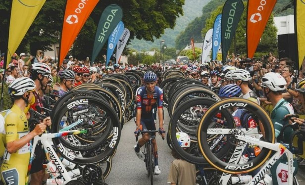 Before the start of today's stage, Romain Bardet receives a salute from the other riders. He cycles towards the camera, flanked on both sides by riders raising their front wheels in acknowledgement of his last race as a professional rider.