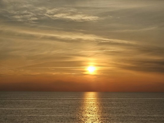 Yellow-orange sunset reflecting on sea surface. There are some clouds on the sky