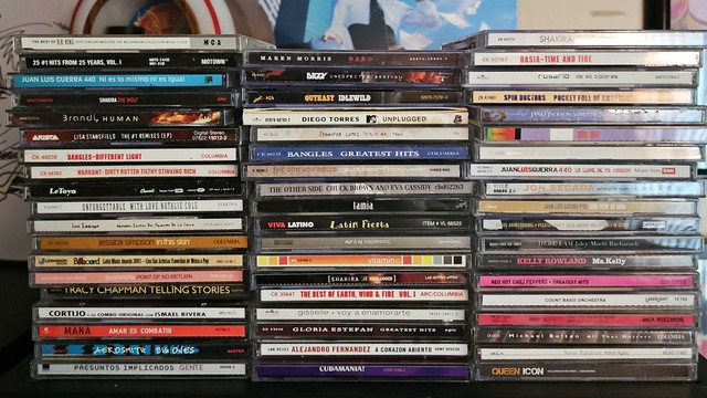 3 stacks of CDs on a shelf, featuring artists like Bangles, Outkast, Mana, Jennifer Lopez, Spin Doctors, Kelly Rowland, and more!