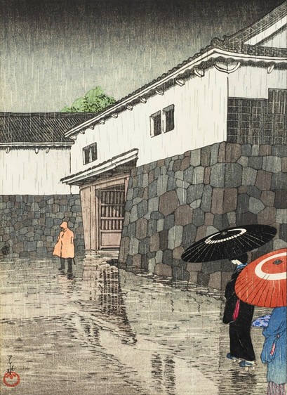 A rainy day by one of the gates at Okayama Castle. On our right, two female figures in kimono, one wearing black and the other blue, hold bamboo umbrellas over their heads as they approach the gate. The courtyard is contained by the heavy stone foundations of the castle; above this, the castle walls of the upper levels are white plaster. Up ahead, a third figure stands in the rain by the gate, wearing a yellow poncho. The ground in front of the gate is slick with rain; overhead, the sky is gloomy and overcast.