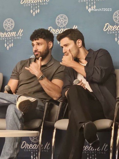 Rafael Silva (Carlos) and Ronan Rubinstein (T.K.) sitting next to each other on stage of the First Responders Reunion Convention V in France. Both are doing a "smolder" (TM) into the camera and making the Shaka sign with their hands in a friendly gesture.