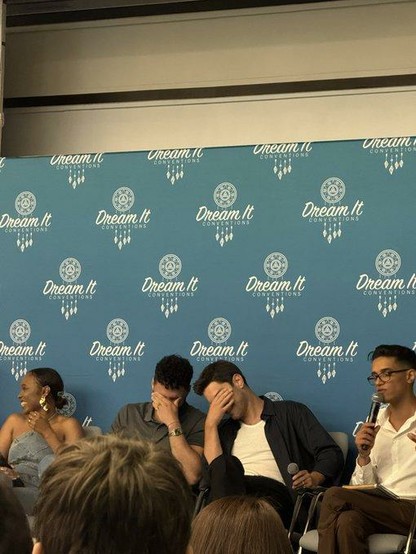 Rafael Silva (Carlos) and Ronan Rubinstein (T.K.) sitting next to each other on stage of the First Responders Reunion Convention V in France. They are laughing like crazy and both hide their eyes behind their hand because they can't calm down from all the giggles.