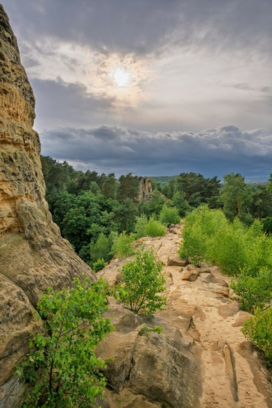 Blick über die Sandstein Klippen in die Ferne auf den Wald dahinter und den Wolkenhimmel. Die Sonne bricht durch den Wolkenhimmel durch.