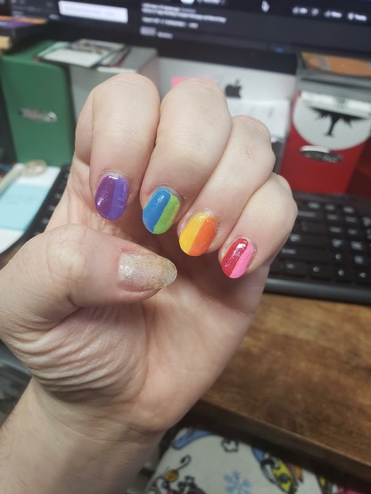 a photo of my painted nails, the four fingers each have two colours (split vertically down the middle), using all 8 colours of Gilbert Baker's pride flag. the thumb is a mix of holographic and opalescent sparklies