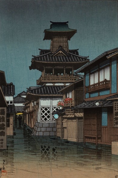 Rain falls on a quiet street somewhere in Okayama, Japan. On our right, the windows of houses are shut; pots of flowers sit out on a narrow second-story balcony and an adjacent rooftop, catching the rain. Up ahead, a temple bell tower stands tall against an overcast sky. Further on, as the street narrows to the width of a little lane, a single figure carries a yellow umbrella over their head as they walk away from us. In the foreground, the rain-slicked street reflects the scene.