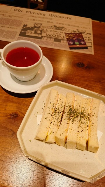 ゾボというナイジェリアのお茶と軽食のサンドイッチ。奥にあるのはゲーム中に登場する新聞をモチーフにしたランチョンマットとガラ（狼男版）のカード