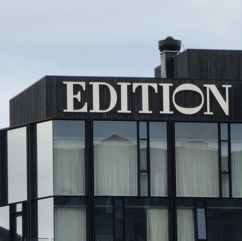 Photograph of a large sign on top of a building in a medium contrast, serif font that says 'EDITION' the O is on its side and is larger proportions to make it's width equal to the hieght of the other letters.