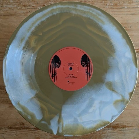 Eine runde Vinyl-Schallplatte mit einem einzigartigen goldenen und weißen Wirbel-Design. Das Etikett in der Mitte ist orange und trägt den Text "AGUSA HÖGTID" sowie die Titelangaben, einschließlich "Sida A" und die Namen der Künstler.