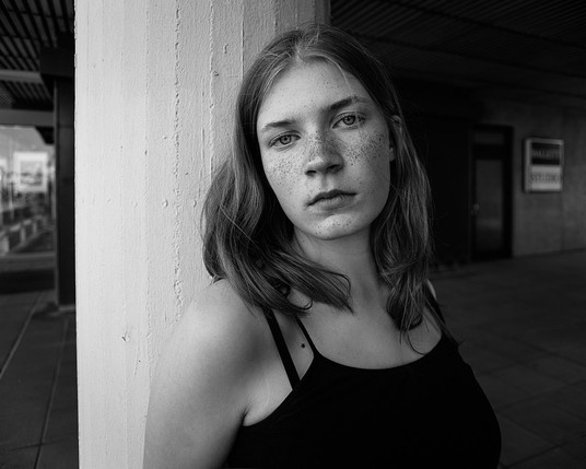 Urban portrait of a 15yo girl with freckles standing on a column.
