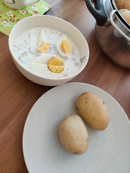 A bowl of polish cold cucumber soup served with a hard boiled egg and a plate with boiled young potatoes.