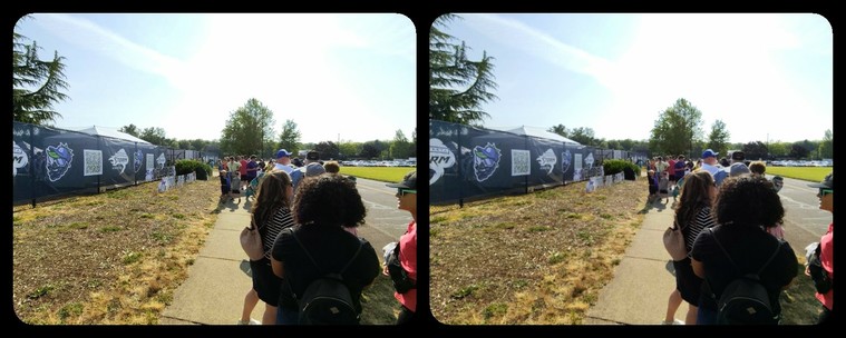 Stereoscopic image. There's a queue of people on the right, and a fence on the left.