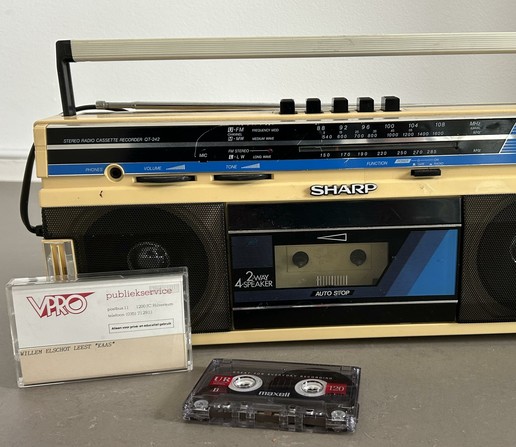 A vintage Sharp stereo cassette recorder with a cassette tape compartment and FM/AM tuning dials is displayed. Next to it are two cassette tapes, one labeled "Willem Elschot leest 'Kaas'" and a Maxell cassette.