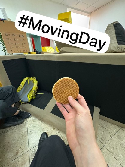 a hand holding up a stroopwafel in front of a disassembled couch