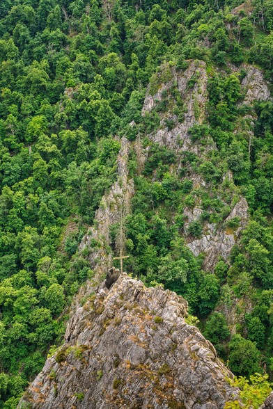 Scharfkantige Felsen bewachsen mit Bäumen auf einem der Felsen steht ein Kreuz