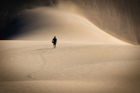 un uomo cammina in un deserto andando incontro ad una gigantesca duna
