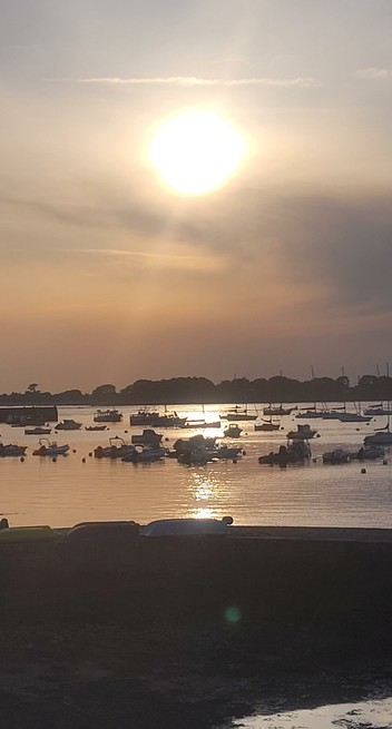 Sonnenuntergang in einem kleinen Hafen in der Bretagne. Es zeichnen sich zahlreiche Boote als Silhouette auf dem Wasser ab, im Hintergrund eine Landzunge, die Sonne spiegelt sich glitzernd auf dem Wasser
