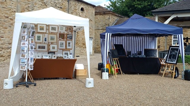 Two gazebos in a courtyard between stone buildings. Artwork is displayed on screens and easels inside